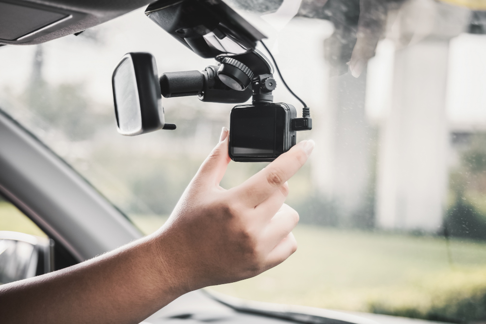 A driver adjusting their rearview mirror which also has a Dashcam attached to it