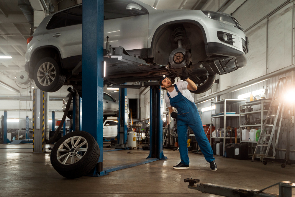 A car mechanic under the car inspecting a potential tune-up with one wheel off